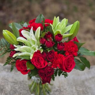 An elegant bouquet in a vase with burgundy spray roses, lilies and dianthus