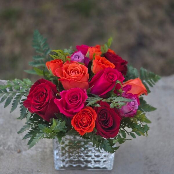 Colorful rose bouquet with red orange and hot pink roses in a square glass vase