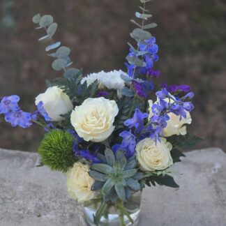 A bouquet in a glass vase with a white rose and blue delphinium