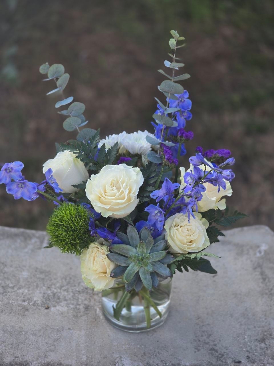 A bouquet in a glass vase with a white rose and blue delphinium