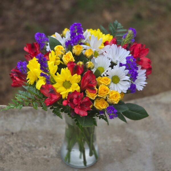 Yellow rose and chrysanthemum bouquet with blue statice, red alstroemeria and fern in a clear glass vase