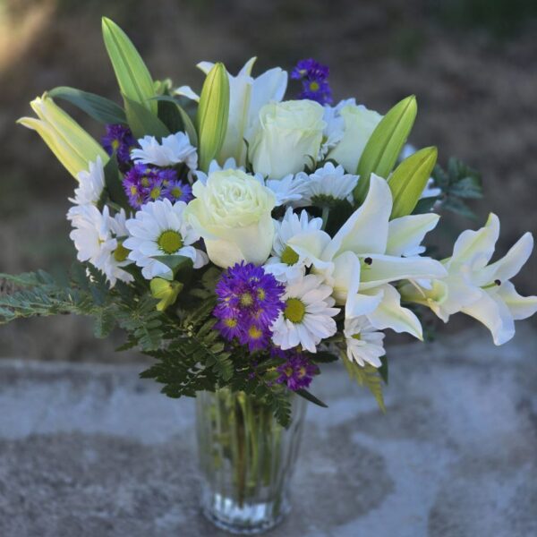 White lily and rose bouquet with white chrysanthemums, fern and greenery in a clear glass vase
