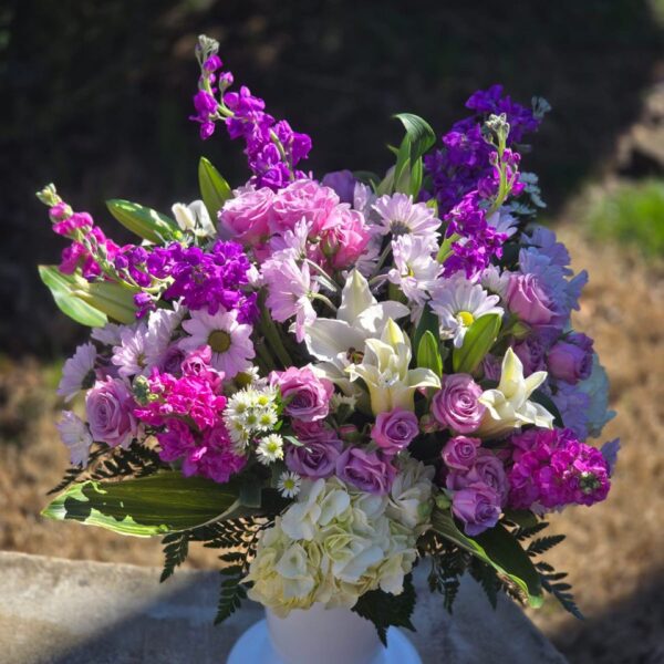 Pink hydrangea and white lily bouquet with lilac matthiola, pink spray roses and greenery in a glass vase
