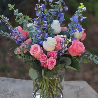 A bouquet in a glass vase with pink spray roses, white and pink roses, delphinium, eucalyptus and mixed grass