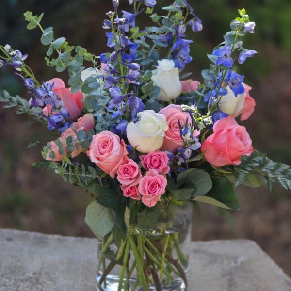 Pink and white flower bouquet with pink spray roses, roses, delphinium and eucalyptus in a glass vase