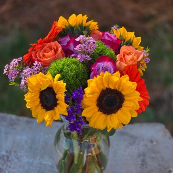 Sunflower and orange flower arrangement with sunflowers, orange gerbera, roses, dianthus, Chamelacium and statice in a glass vase
