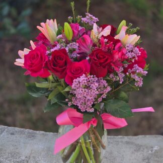 A bouquet in a glass vase with red and pink roses, a pink lily and a chamelacium