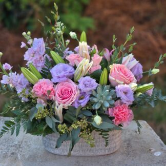 A bouquet in a wicker basket with pink lilies, purple eustoma, pink matthiola, spray roses, pink roses, carnations