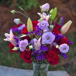 A bouquet in a glass vase with a pink lily, a red rose, eustoma and statice