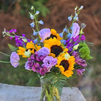 A bouquet in a glass vase with sunflowers, purple eustoma, green dianthus, lilac matthiola and alstroemeria
