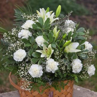 A bouquet in a wicker basket with white carnations, white lilies, limonium and mixed grass – tenderness, purity and durability in every petal