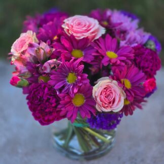 A bouquet in a glass vase with daisies, purple carnations, alstroemeria, pink roses and statice