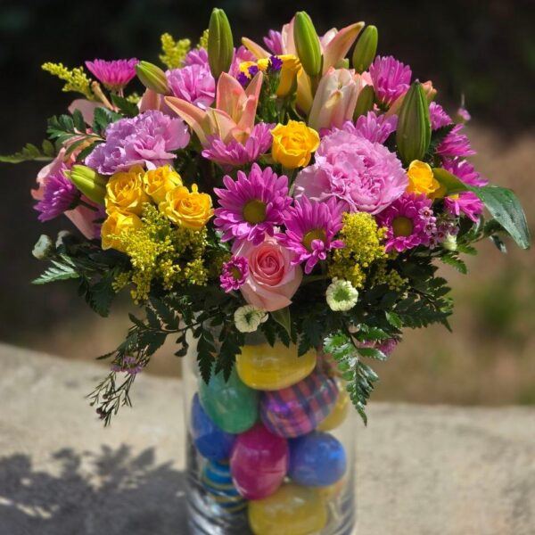 Easter flower arrangement with fresh lilies and roses in a glass cylinder with decorative Easter eggs