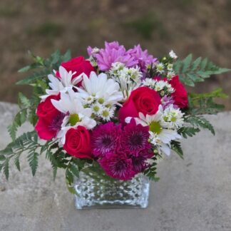 A bouquet in a glass vase with a rose, multi-colored chrysanthemum, daisy and fern