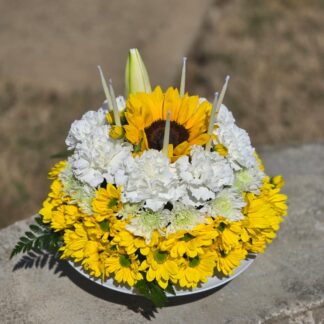 A cake bouquet on a floral foam with yellow spray chrysanthemum, white carnation, lily, sunflower, fern and candles – a celebration of light, color and aroma