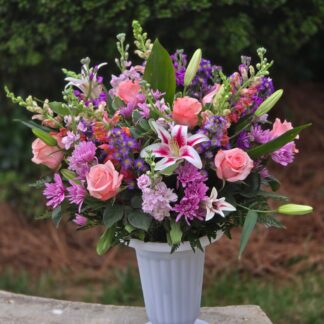 Business bouquet in a white plastic vase with lilies, pink roses, matthiola, spray chrysanthemum, Monte Cosino, and ferns.
