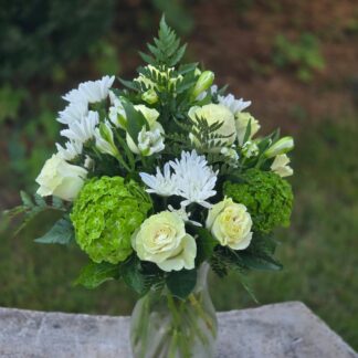 A bouquet in a glass vase with a white rose, green hydrangea, and white spray chrysanthemum