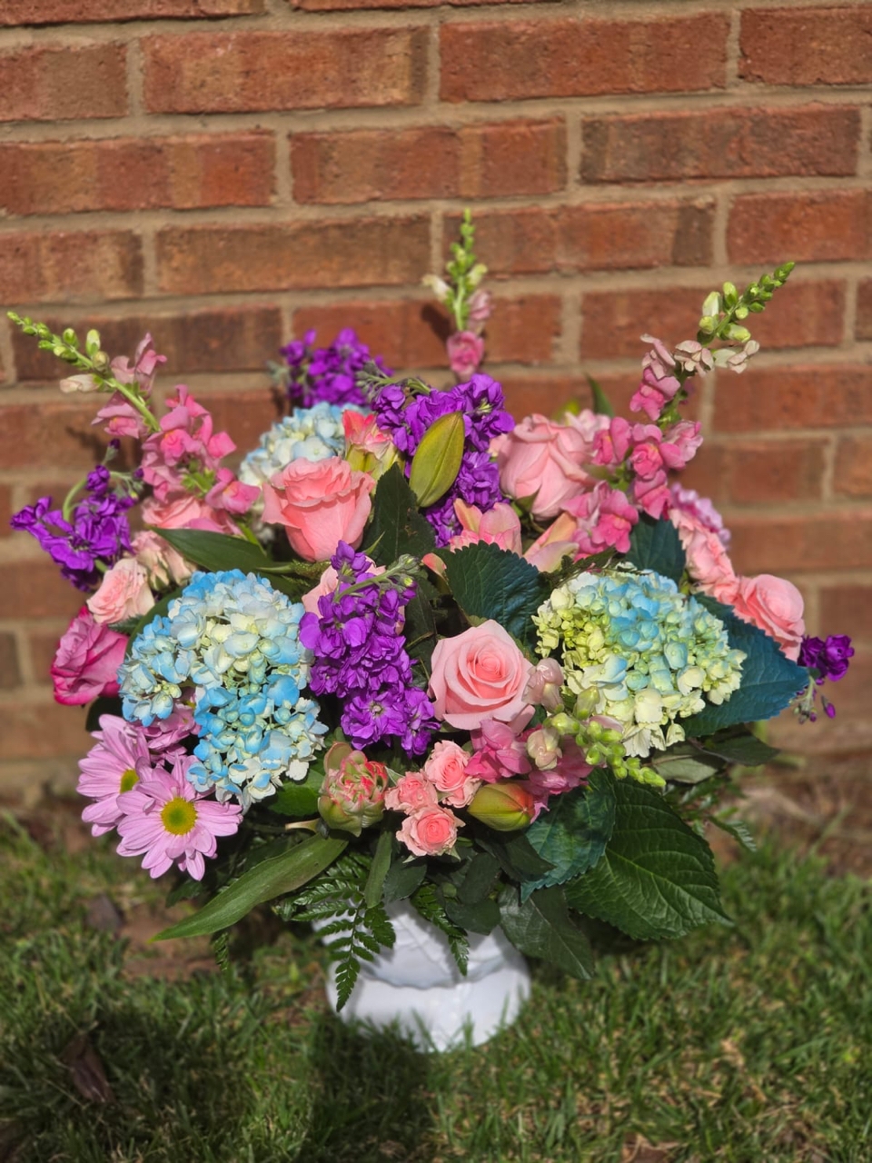 A bouquet in a white vase with blue hydrangea, pink roses, gerbera, and matthiola