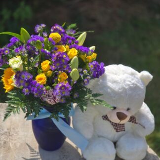 A bouquet in a blue glass vase with a yellow spray rose with White Teddy Bear